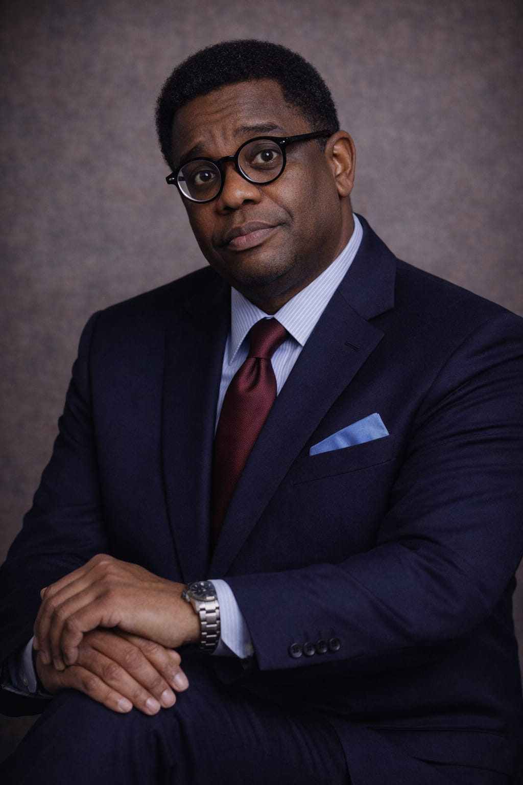 Formal portrait of a man in a dark suit with a purple tie and pocket square.